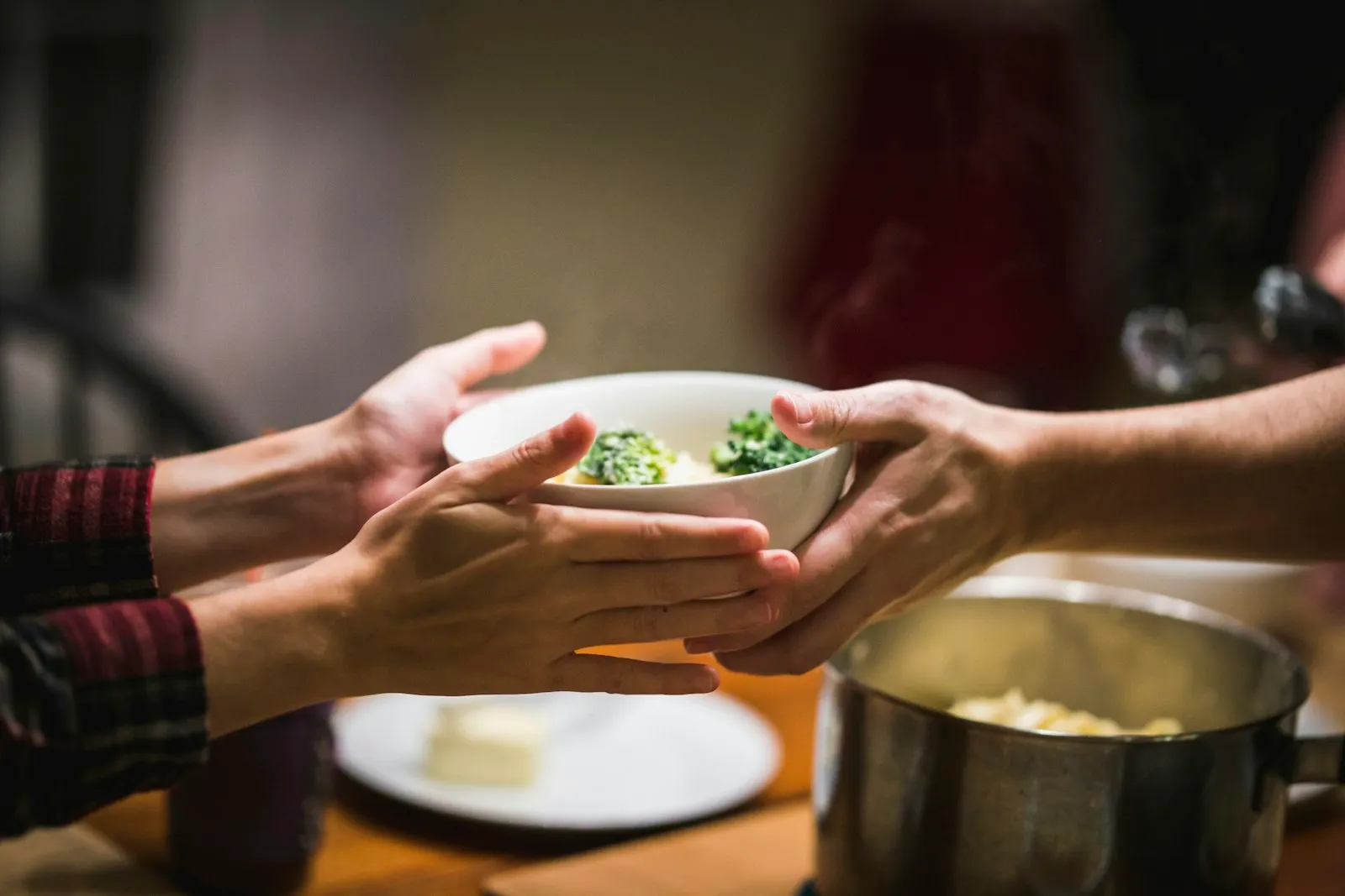 Two pairs of hands passing a bowl of food across a table
